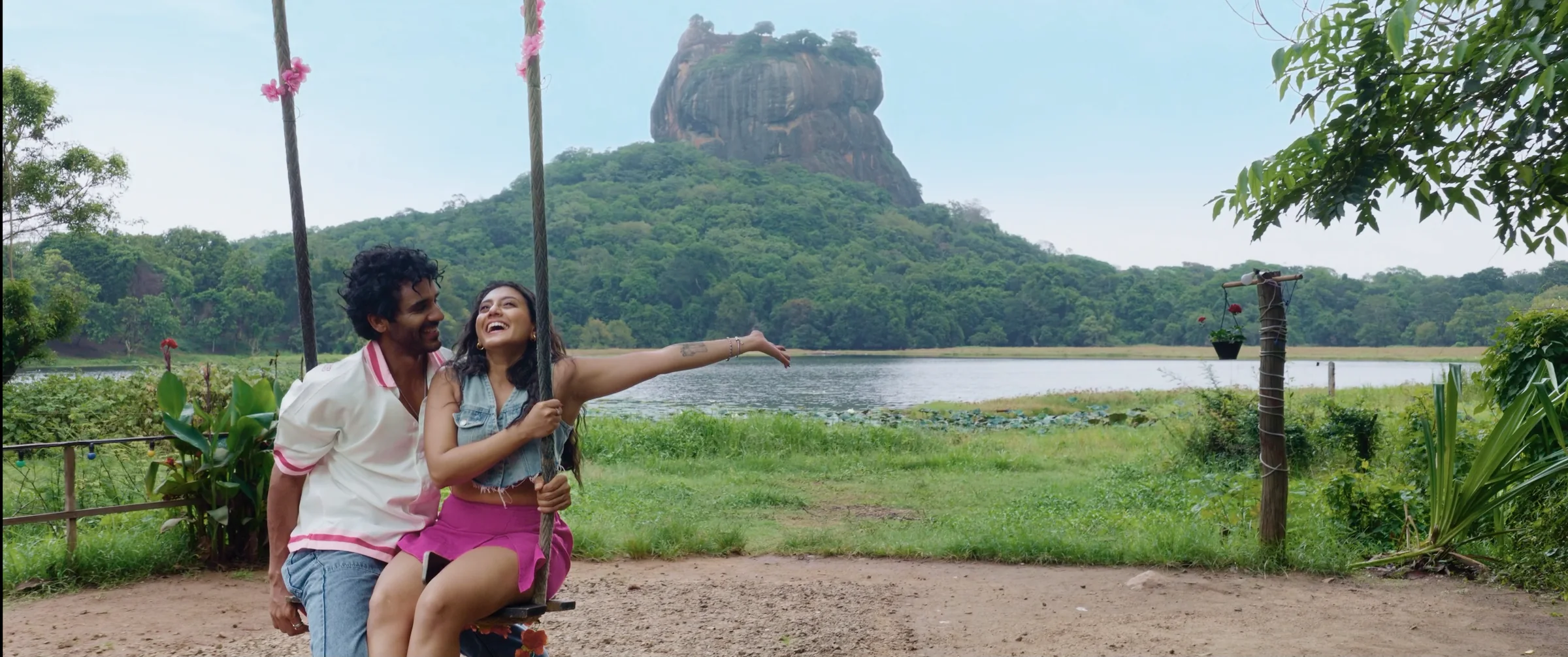 A couple on a swing beside a lake, with a rock rising in the distance